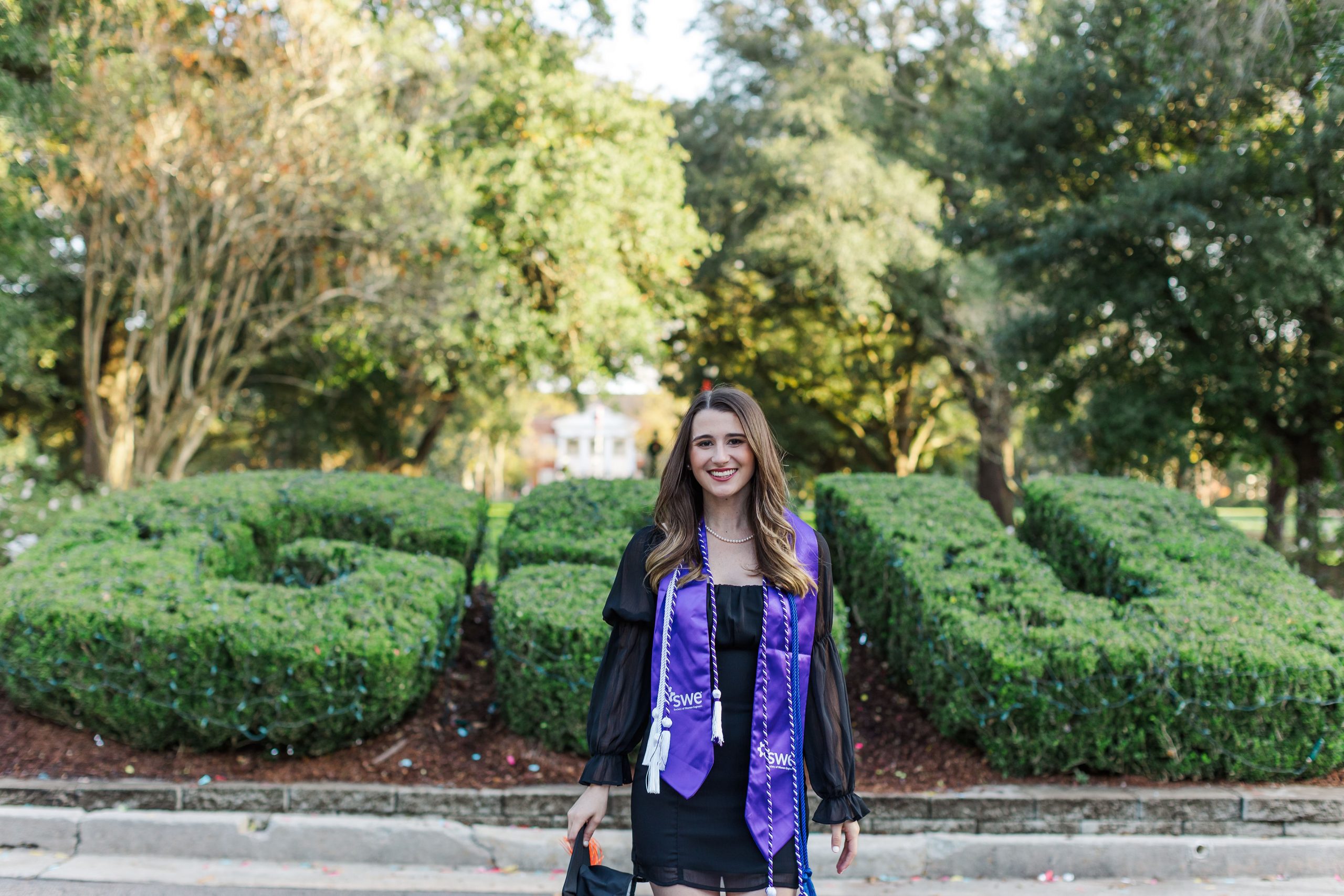 Photo of Lydia Poole in graduation attire in front of GSU bushes. Photo Credit: Rebecka Jane Photography