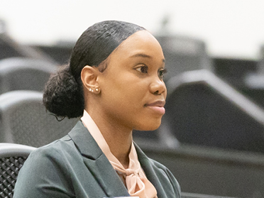 A student in a business suit sitting in a classroom looking at the front of the room.