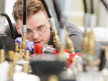 A student works with mechanical equipment while wearing safety glasses.