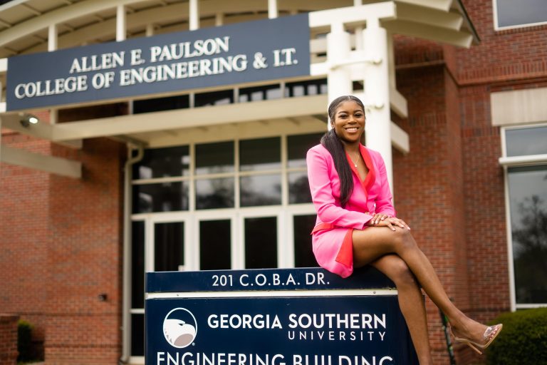 Smiling female student in a pink dress sitting on the Georgia Southern University Engineering Building sign.