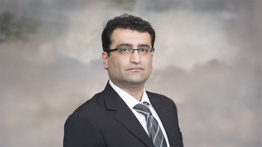 Professional headshot of a man in a dark suit and striped tie, wearing glasses, against a neutral backdrop.