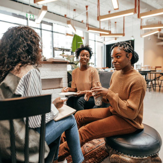 Three women sitting and talking together in a modern office or coworking lounge area.