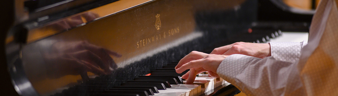 A close-up view of a musician's hands playing a Steinway & Sons grand piano.
