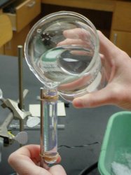 Clear liquid being poured from a glass beaker into a test tube secured by a laboratory stand.