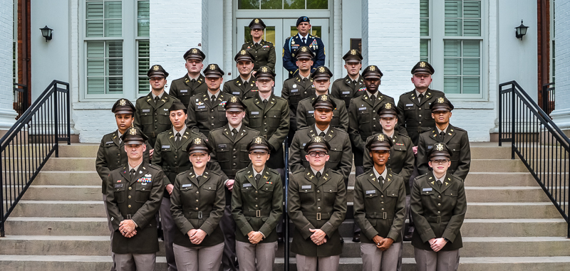 Group of military officers or cadets in service dress uniforms posing for a formal portrait on the stairs of a building.