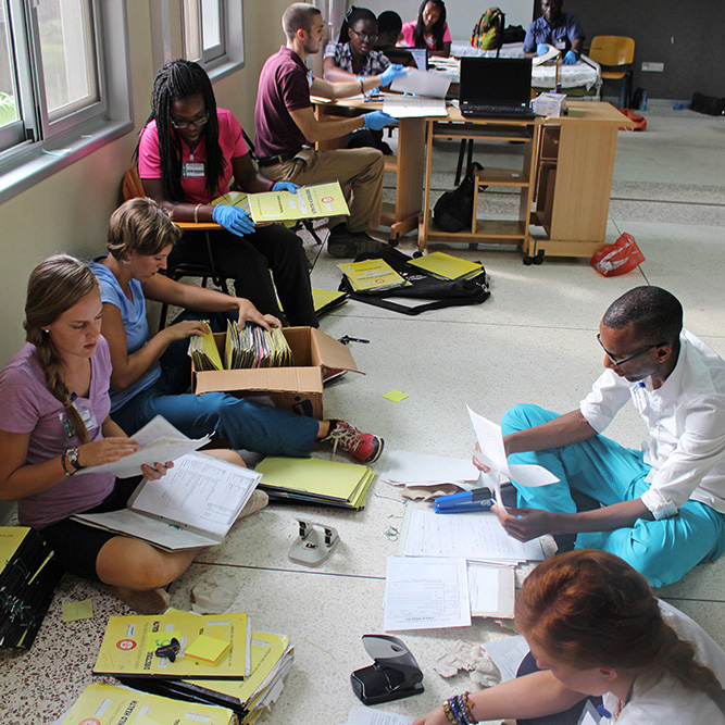A diverse group of healthcare students or aid workers sitting on the floor sorting through medical charts, files, and folders.
