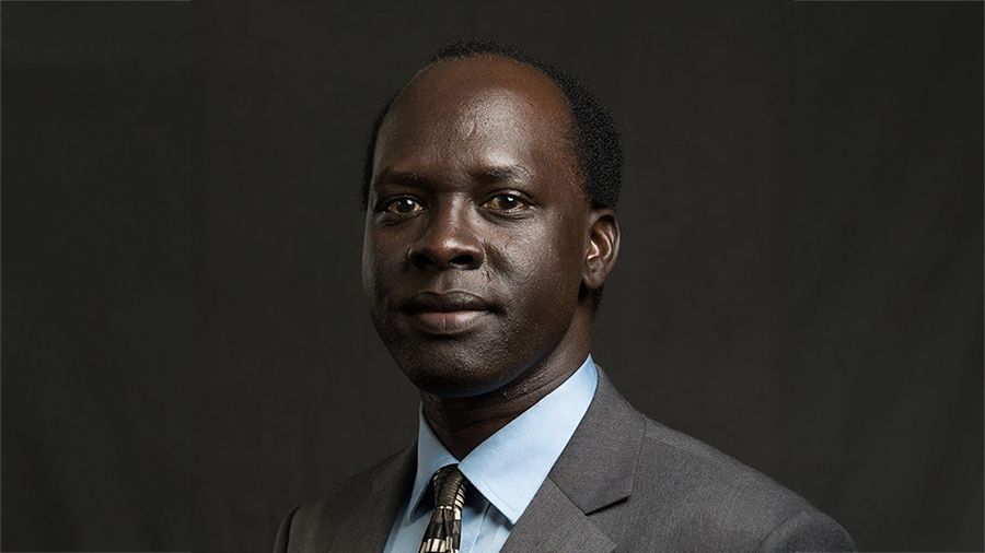 Professional head-and-shoulders portrait of a man in a gray suit and light blue shirt against a dark background.