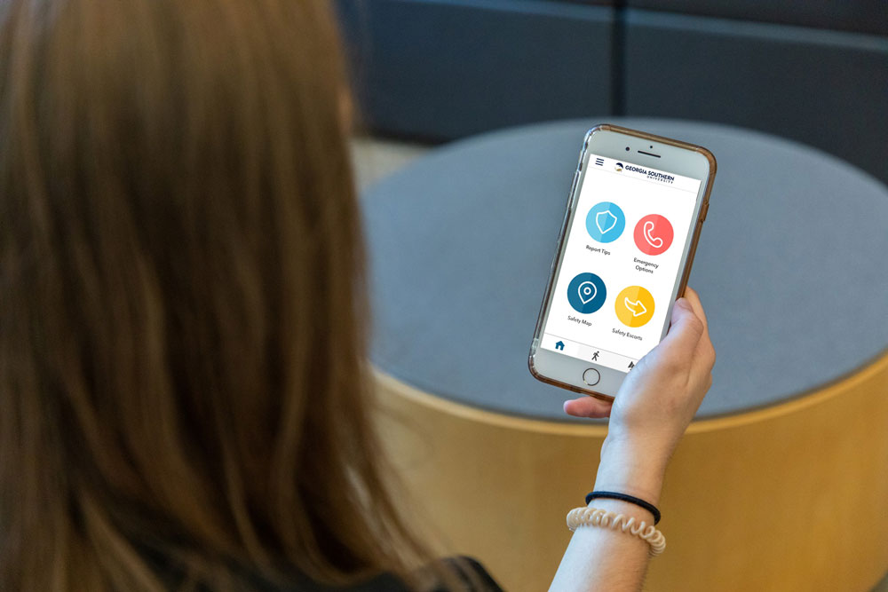 An over-the-shoulder view of a person holding a smartphone displaying the Georgia Southern University campus safety app interface.
