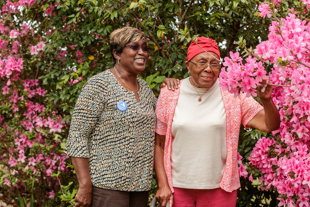 An older lady accompanied by a caretaker in a garden