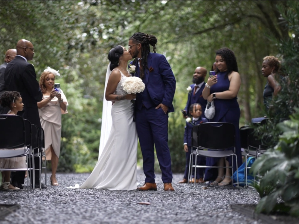 A newly married bride and groom sharing a romantic first kiss at the altar during an outdoor wedding ceremony on a gravel path.