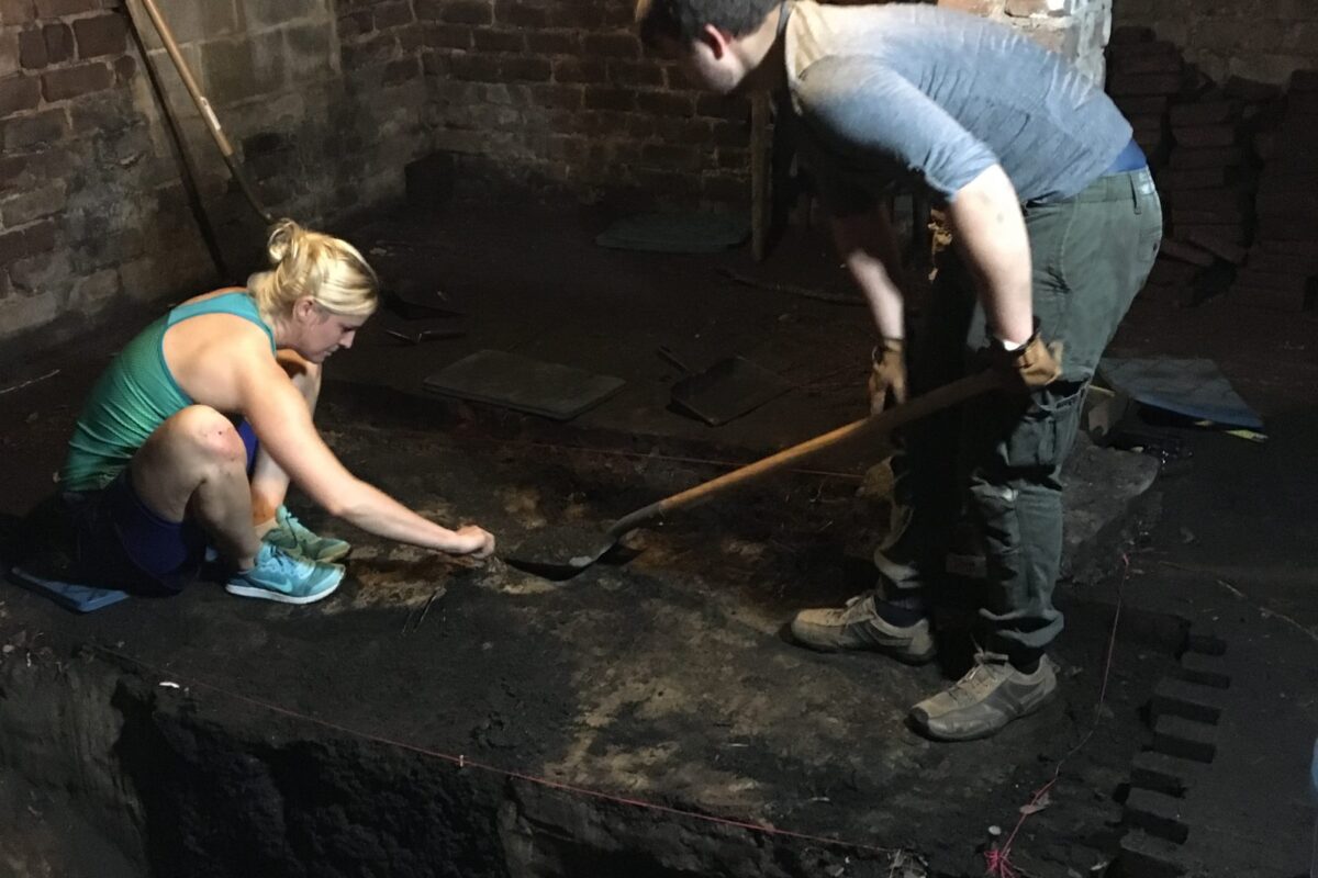 A man and woman work at an archaeological dig site inside an old building.