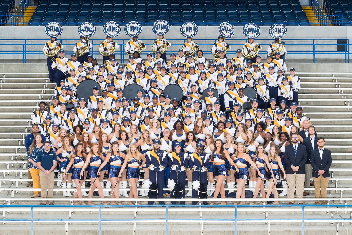 The Georgia Southern University Marching Band poses for a large group portrait in uniform on stadium bleachers.