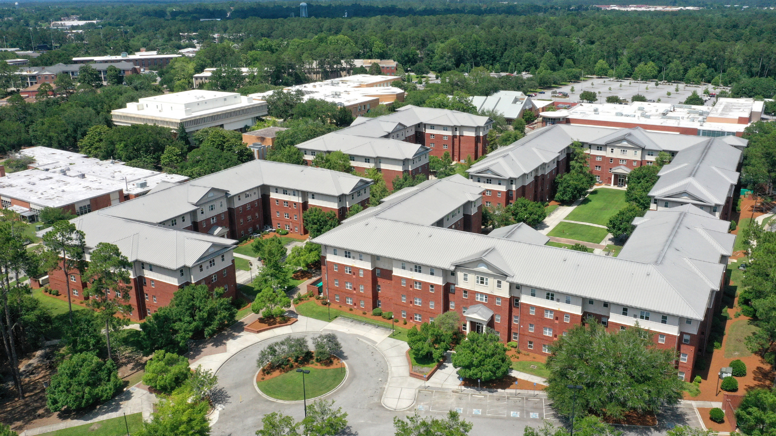 Sweeping aerial overview showcasing the Centennial Place residential complex, with its large brick buildings and gray metal roofs arranged around a prominent circular driveway turnaround.