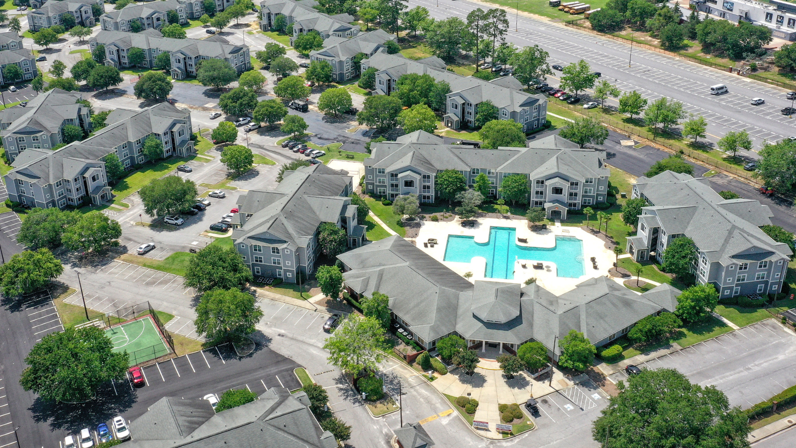 High-angle aerial drone photograph showcasing the massive campus apartment complex with gray shingled roofs, U-shaped courtyards, and surrounding green pine trees.