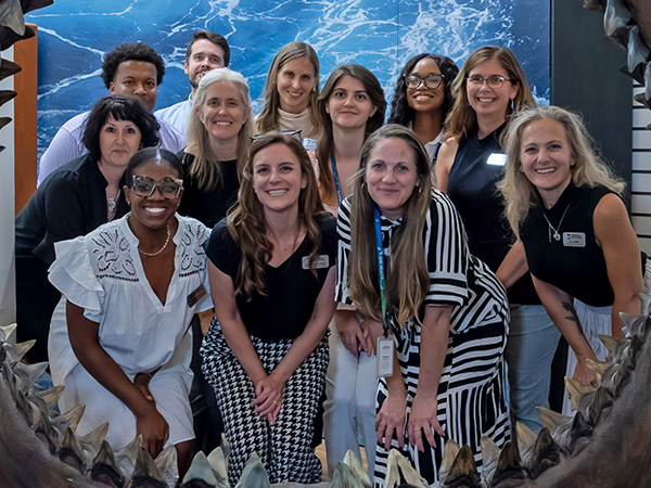 A diverse group of professional colleagues smiling together for a group photo in front of a blue background with wave patterns.