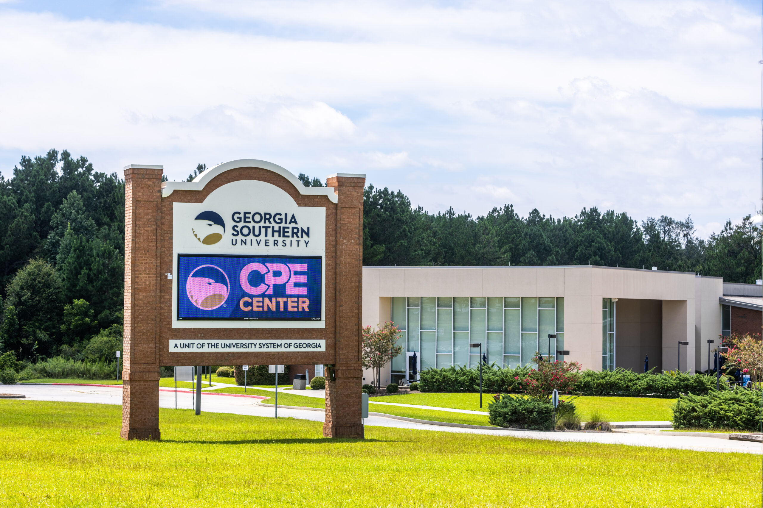 A brick and white Georgia Southern University monument sign stands on a grassy campus lawn, featuring a digital display for the CPE Center in front of a modern academic building and a dense treeline.