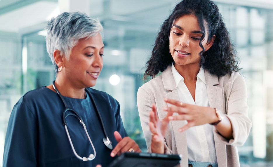 Two healthcare professionals review information on a tablet during a patient consultation in a bright clinic setting.