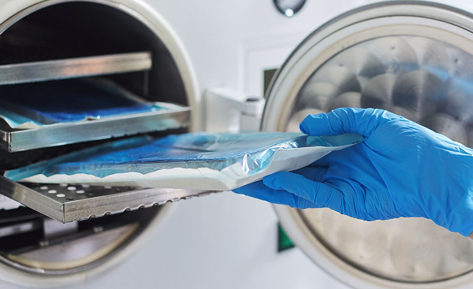 Gloved hand inserting a sealed medical sterilization pouch into an autoclave for sterilization.