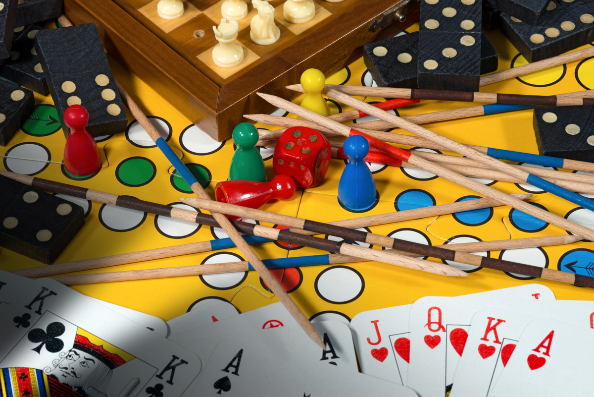 Colorful assortment of board game pieces, dice, dominoes, and playing cards scattered on a yellow game board.