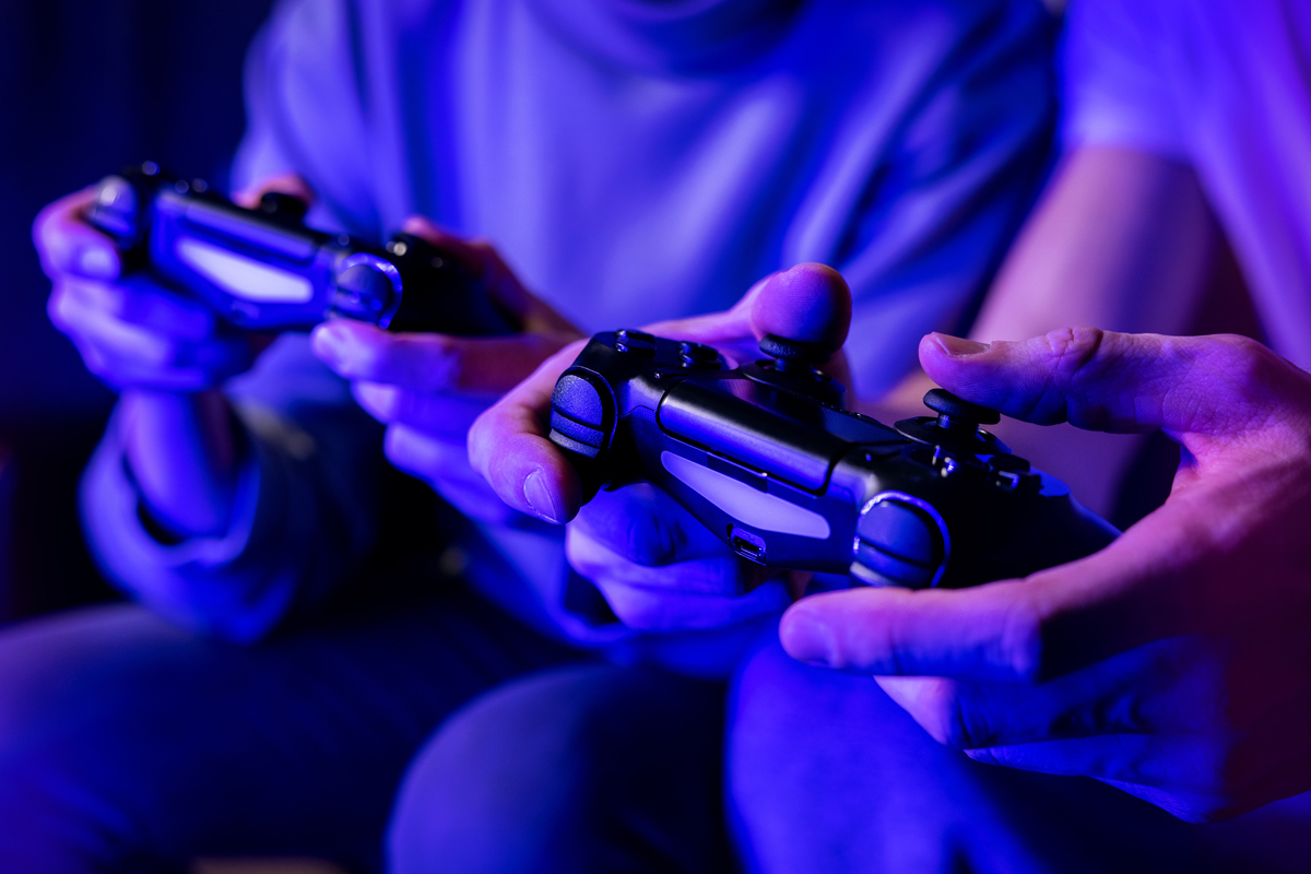 Two people gaming with wireless controllers in a blue-lit room.