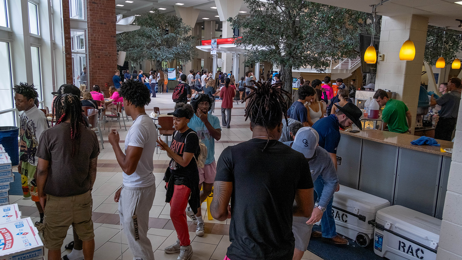 Crowded campus cafeteria or student center with a long service counter and students waiting in line.