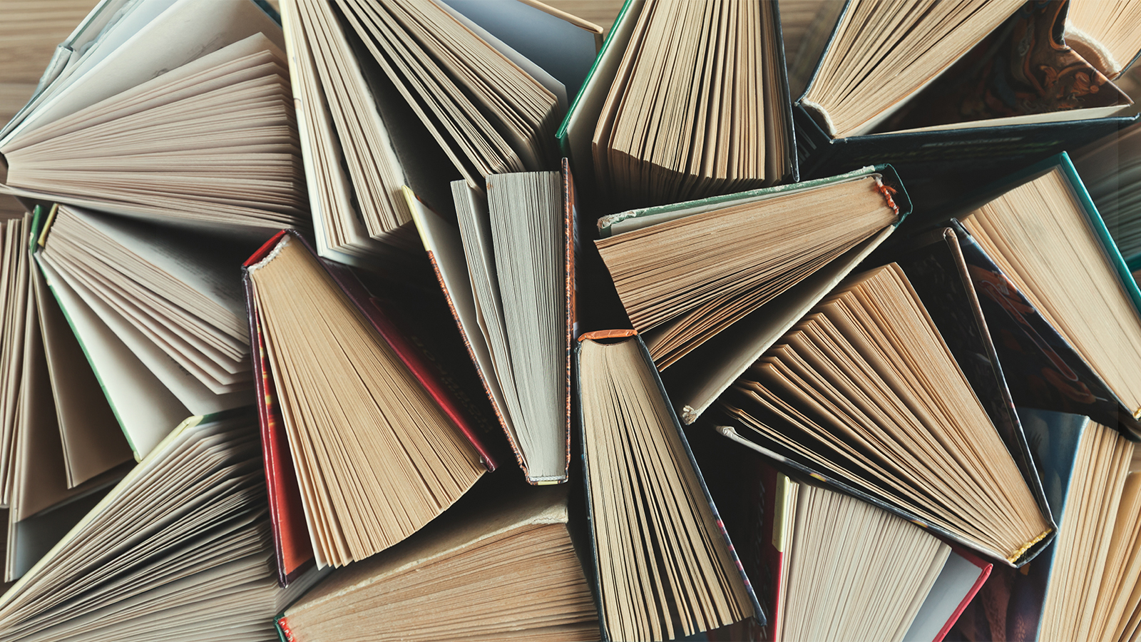 Aerial view of a clutter of open and closed books stacked together on a wooden surface.