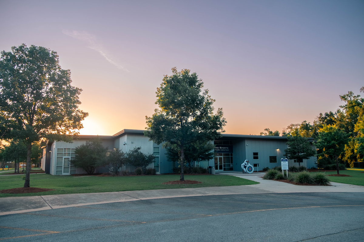 Sunset exterior of a modern campus building with trees and a sidewalk in the foreground, soft orange sky above the entrance.