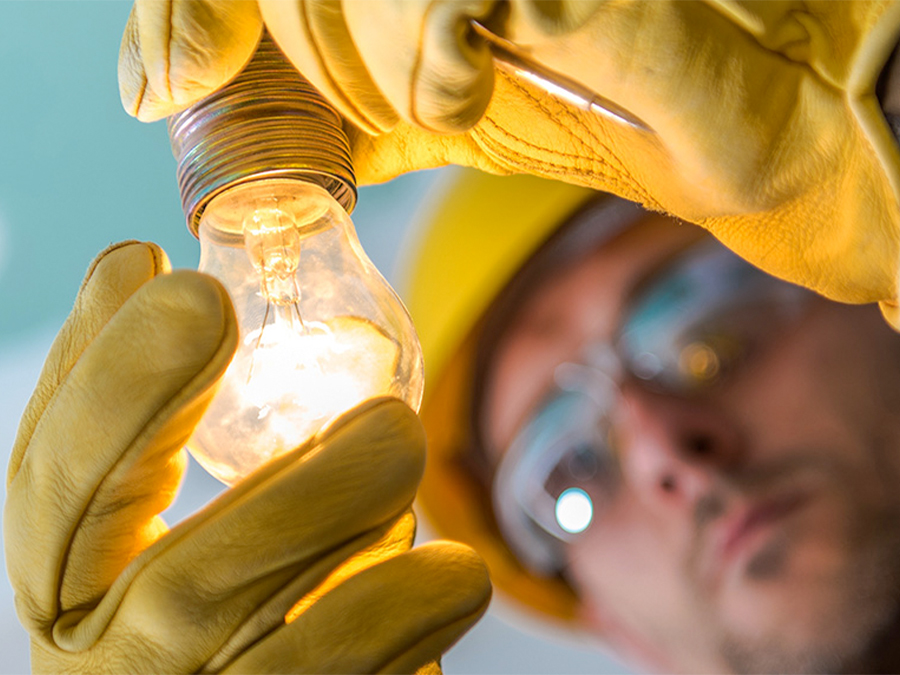Electrician wearing protective work gloves inspecting a glowing light bulb.